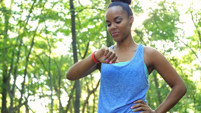 African American athletic woman checking fitbit device after running